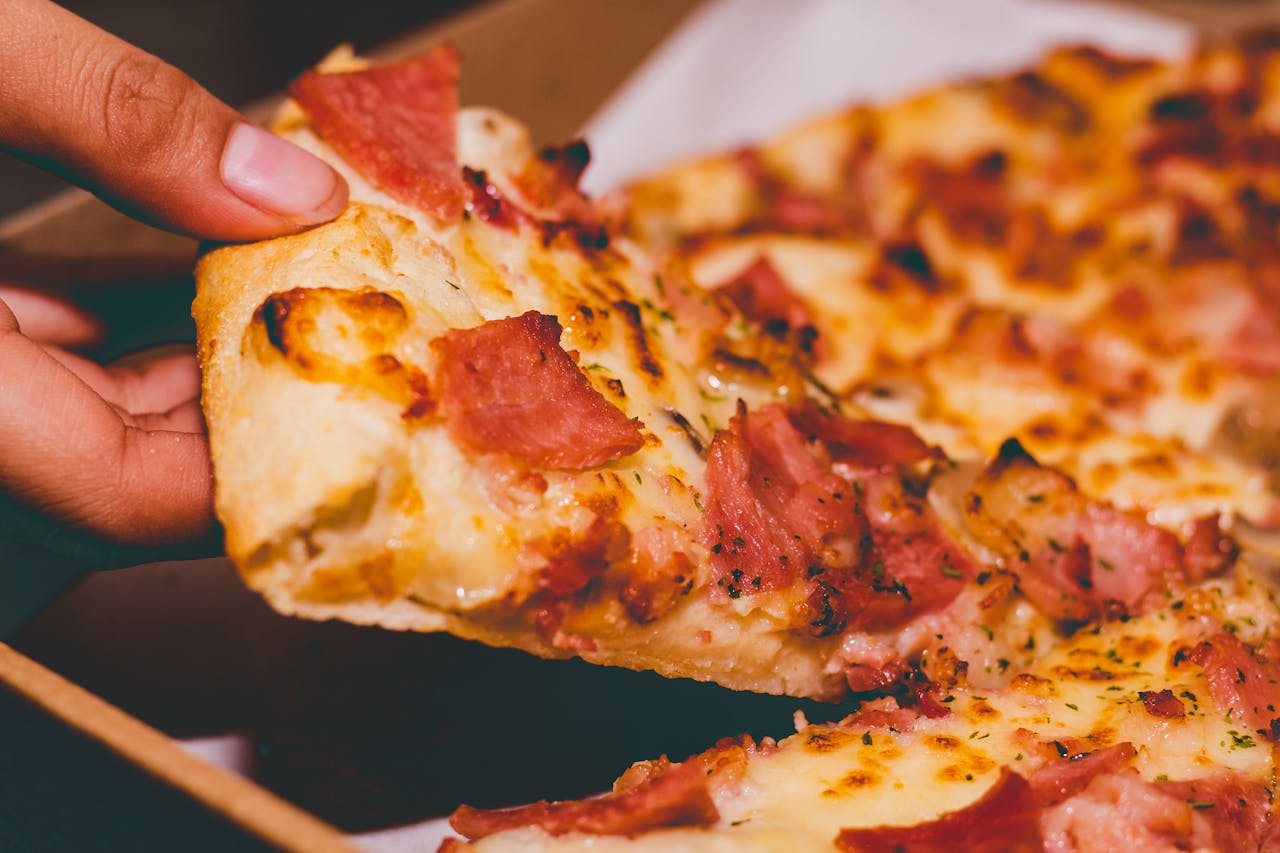 services-bg Close-up of a hand holding a delicious slice of pepperoni pizza.