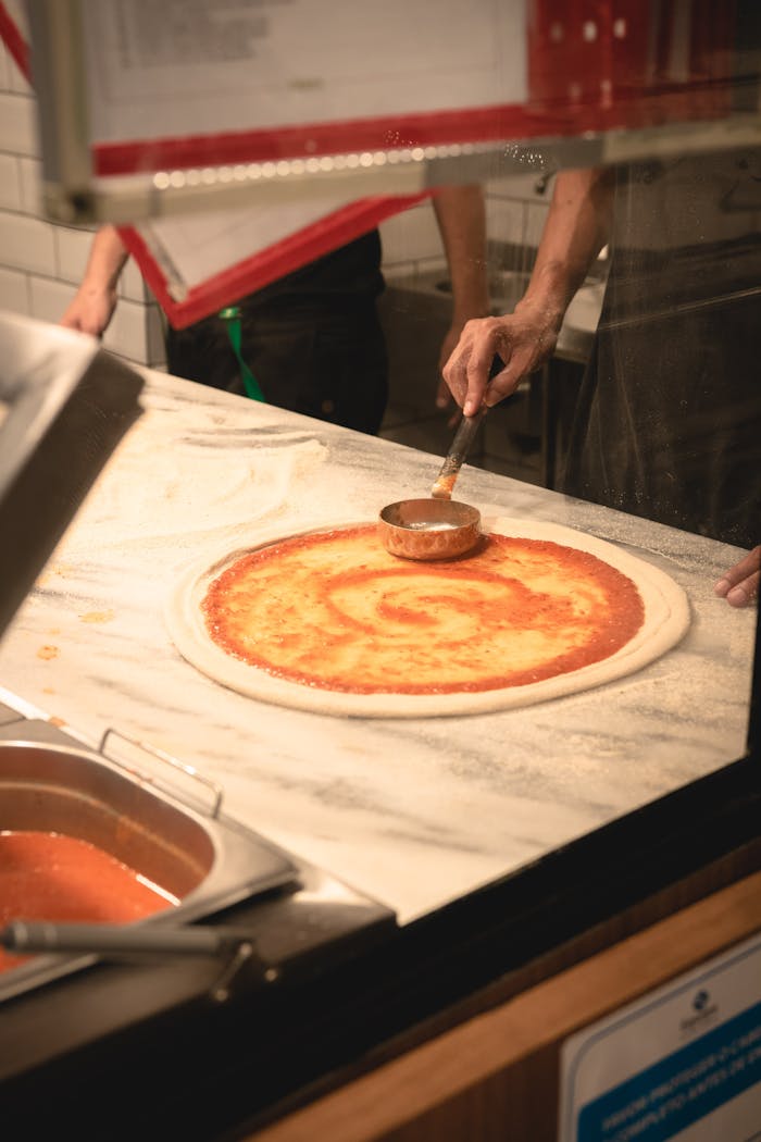 The Art of Drawing Readers In: Your attractive post title goes here Authentic Italian pizza preparation with fresh tomato sauce on dough in a Brazilian kitchen.